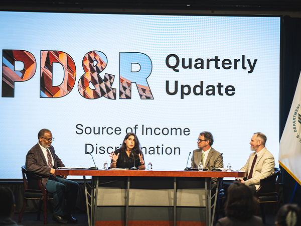 Four panelists sit at a table. A large screen behind them reads "PD&R Quarterly Update: Source of Income Discrimination."