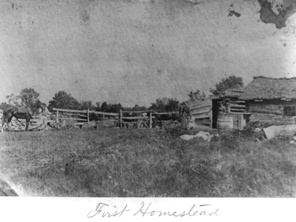 A black and white photograph of a log cabin at the Daniel Freeman homestead in Beatrice, Nebraska. "First Homestead" is written below the photograph.