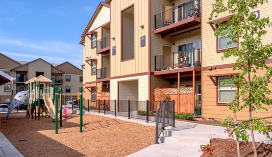 A three-story multifamily building with a playground in the foreground. 