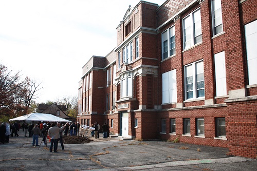 Photograph of the front façade of a three-story brick school building with several windows boarded up.