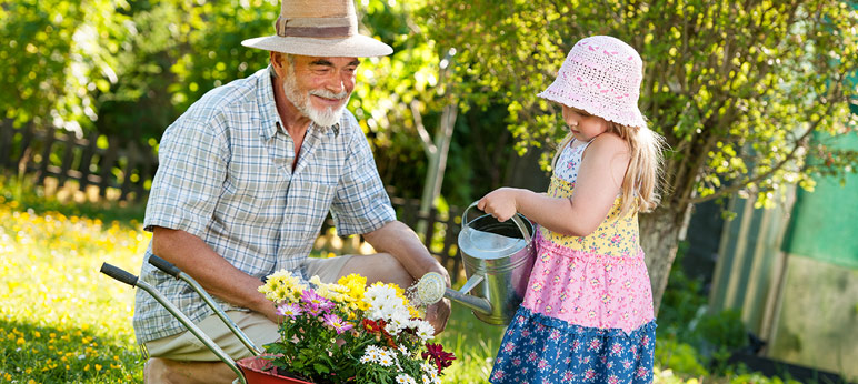 Image of a man and a young girl outside watering flowers with a watering can.