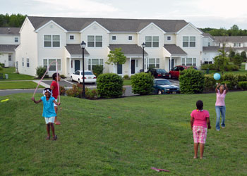 Four children play in a yard adjacent to two-story residential units within the Ethel Lawrence Homes community.
