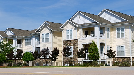 Photograph of a low-rise, multifamily residential building with a façade that includes siding and stone. 