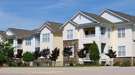 Photograph of a low-rise, multifamily residential building with a façade that includes siding and stone. 