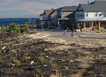 A road circling a Colorado subdivision separates houses from fire damaged land.