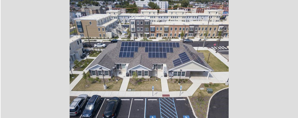 Aerial view of one-story building with solar panels on the roof and low-rise apartment buildings in the background.