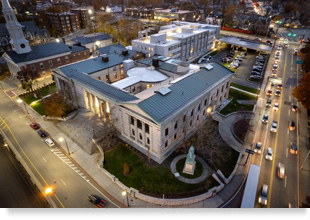 Aerial photograph of the Courthouse Lofts, its principal courthouse building in the foreground and annex building in the background, in the context of the surrounding Lincoln Square neighborhood of Worcester, Massachusetts.