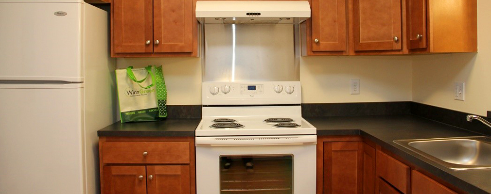 Interior photograph of a kitchen in a residential unit showing a refrigerator, cabinetry, stove with range hood, sink, and dishwasher.