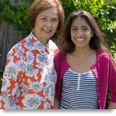 An older woman and a younger woman pose for a photo standing next to each other.