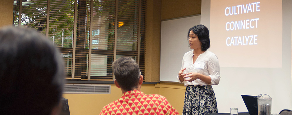 A woman gives a presentation at the front of a classroom.