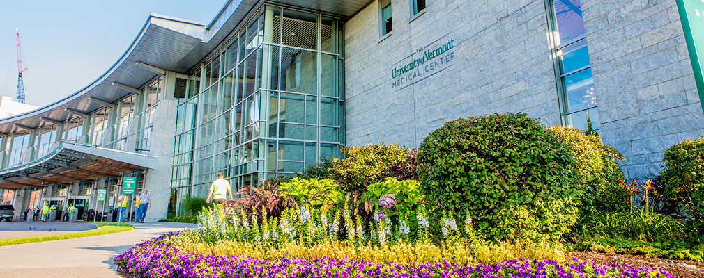 Photograph of the main entrance to the University of Vermont Medical Center, a multistory stone building with the entrance marked by a large glass projection. 