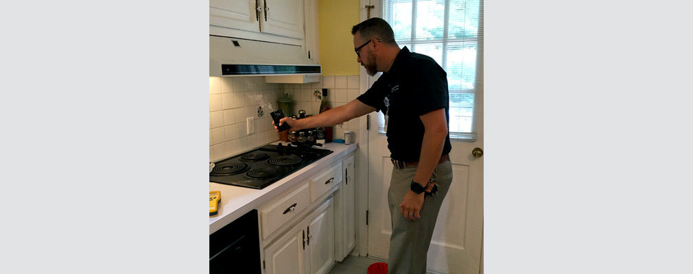 Photograph of a man in a residential kitchen measuring the performance of a stove vent.