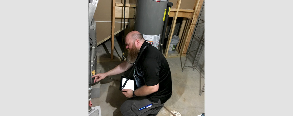 Photograph of a man crouching to examine a furnace in a basement.