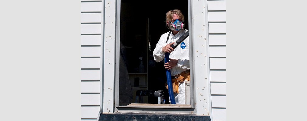 Photograph of a contractor wearing a respirator mask while using a vacuum to clean a window frame.