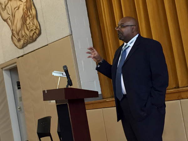 Image of a man speaking behind a podium in an auditorium. Image of a man speaking behind a podium in an auditorium.