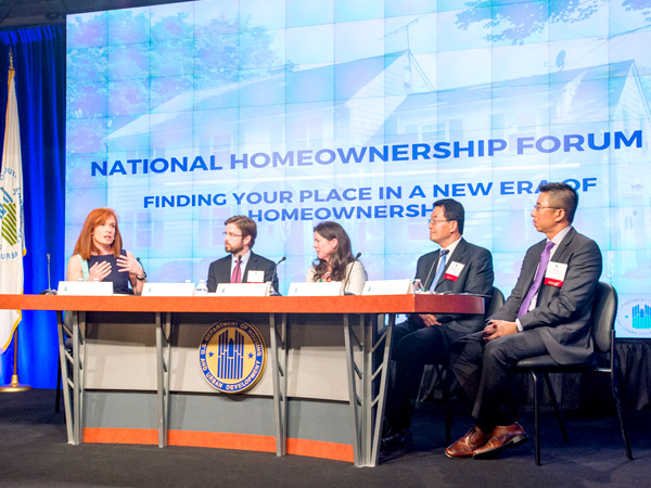 Five individuals, including Diana Olick, Jon Spader, Christie Peale, Lawrence Yun, and Joel Kan (left to right), sit at a table on stage in front of a screen that says “National Homeownership Forum.”