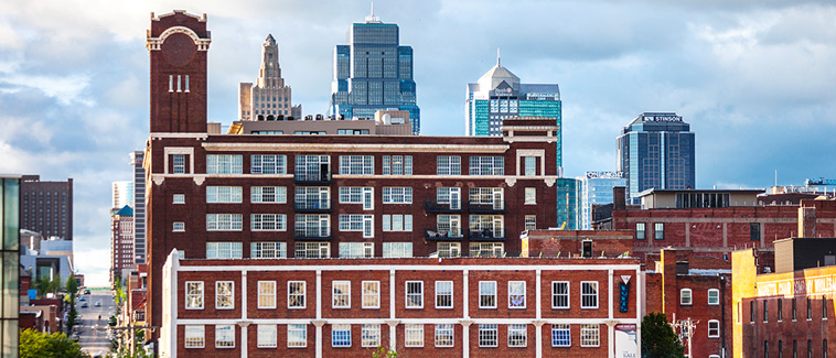 Photograph of several multi-story brick buildings in front of the Kansas City, Missouri skyline.