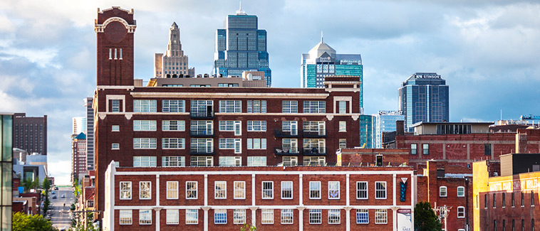 Photograph of several multi-story brick buildings in front of the Kansas City, Missouri skyline. Photograph of several multi-story brick buildings in front of the Kansas City, Missouri skyline.