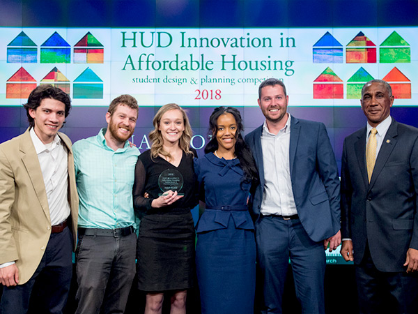 The five students in the University of Maryland, College Park design team and Chris Bourne, HUD senior advisor, stand onstage in front of the 2018 IAH banner.