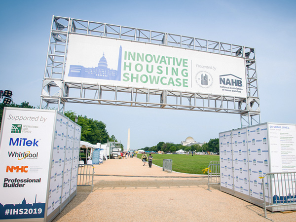 A sign states “Innovative Housing Showcase” and bears the HUD and NAHB logos. Exhibits set up along the National Mall and the Washington Monument are visible in the background. A sign states “Innovative Housing Showcase” and bears the HUD and NAHB logos. Exhibits set up along the National Mall and the Washington Monument are visible in the background.