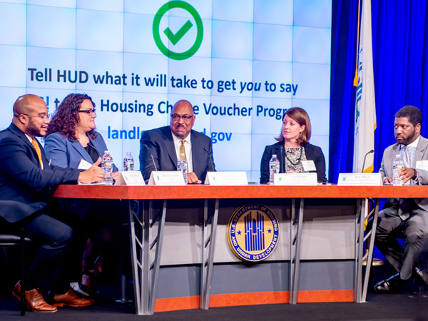 Steven Durham, director of Housing Voucher Programs in HUD’s Office of Public and Indian Housing, sits left of four seated panelists at a table bearing the HUD logo. Steven Durham, director of Housing Voucher Programs in HUD’s Office of Public and Indian Housing, sits left of four seated panelists at a table bearing the HUD logo.