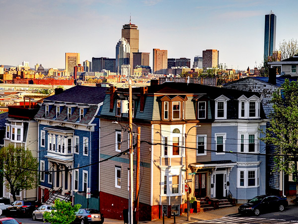 The city of Boston. Multistory townhomes are visible in the foreground, and the skyline of downtown Boston is visible in the background.