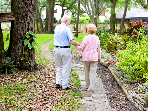 An elderly couple holding hands walking outdoors.