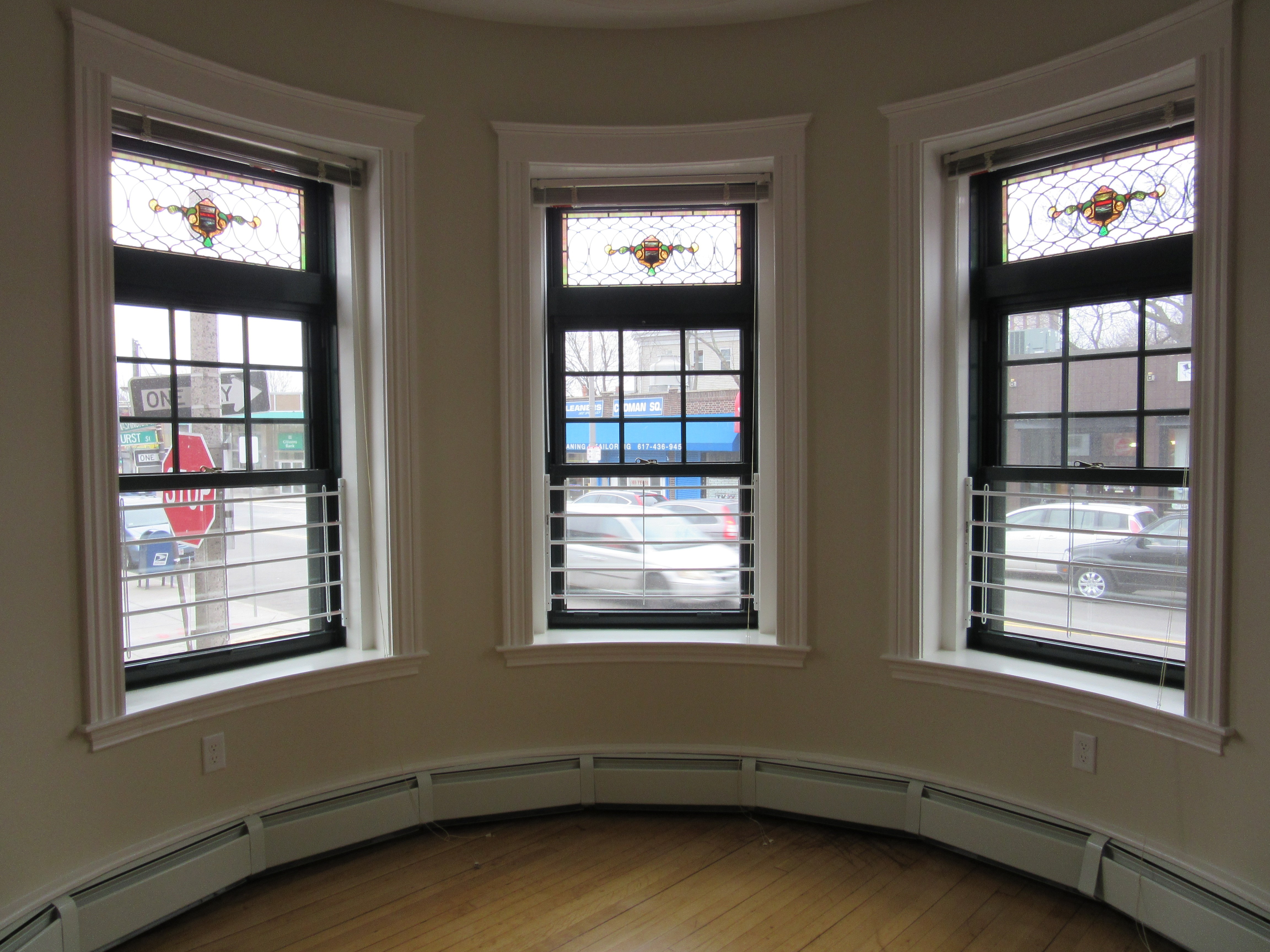 Photograph of the interior of a rehabilitated historic structure in Codman Square’s commercial district, showing a room with three large windows and wood flooring. 
