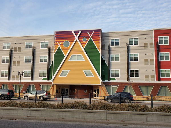Image of a four story apartment building with center of building depicting a stylized teepee in front of mountains.