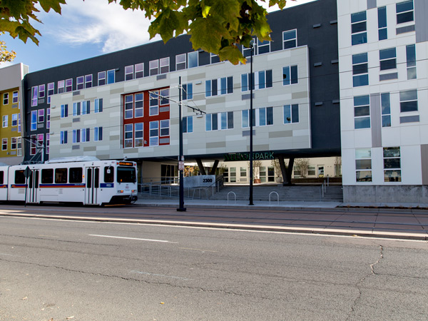 Photograph of the façade of a multi-story apartment building, with a light-rail train passing along a street in front. Photograph of the façade of a multi-story apartment building, with a light-rail train passing along a street in front.