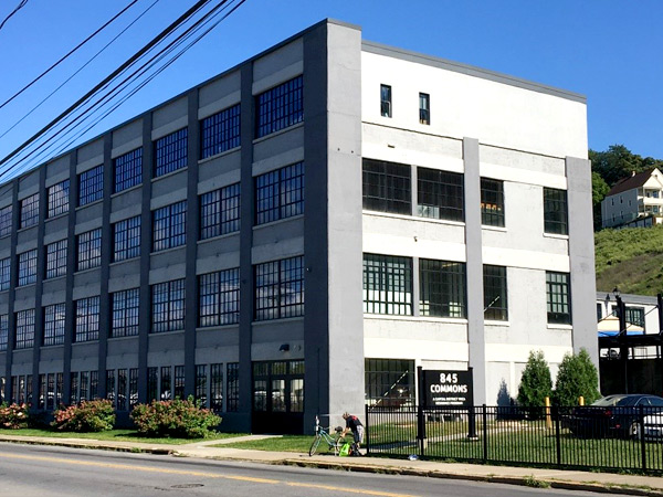 A four-story building with large glass windows and a sign in front that says “845 Commons.” A four-story building with large glass windows and a sign in front that says “845 Commons.”