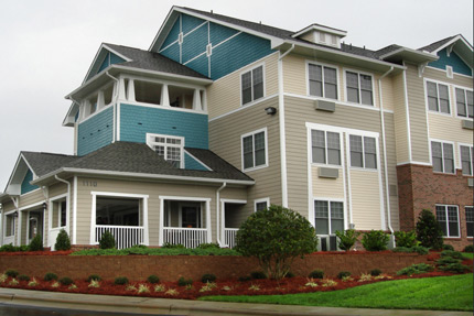 Photograph showing apartment housing facing a street with landscaping in the foreground.