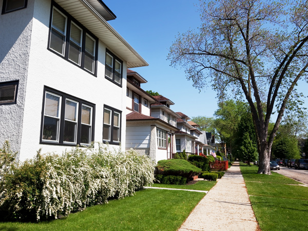 A row of multistory townhomes with front porches line a sidewalk.