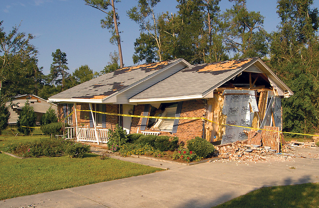 Photo shows a severely damaged single-family brick home with yellow caution tape around it.