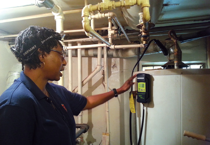 Photo shows a woman examining a hot water heater.