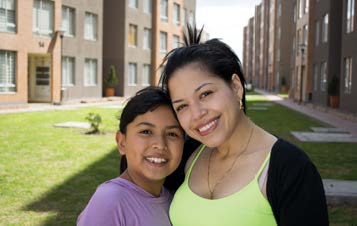 Photo of a woman and young girl smiling in the courtyard of a residential building.