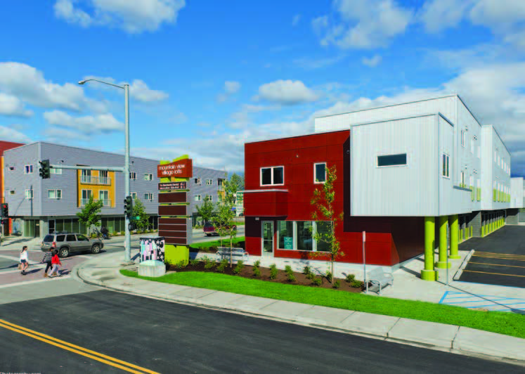 Photo shows two buildings located at crossroads with retail on the first floor and housing above.