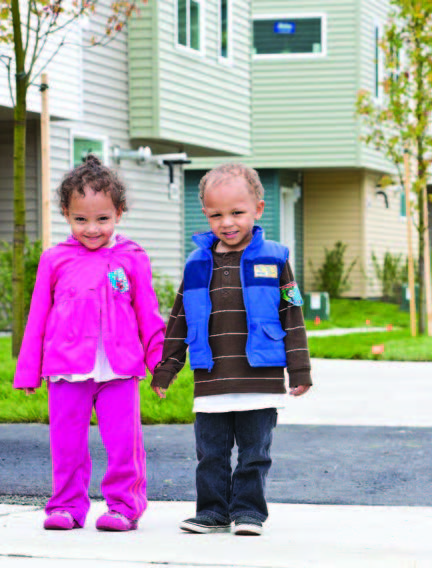 A little boy and girl holding hands standing on a driveway with houses behind them.