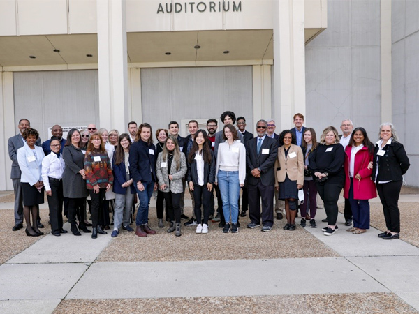 Photo of students, guest speakers, and HUD staff gathered in the plaza in front of an auditorium. Photo of students, guest speakers, and HUD staff gathered in the plaza in front of an auditorium.