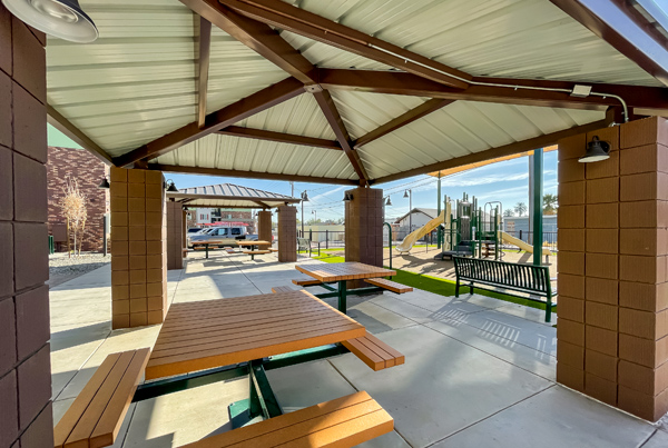 Two ramadas covering picnic tables, a bench, and a playground in the background. Two ramadas covering picnic tables, a bench, and a playground in the background.