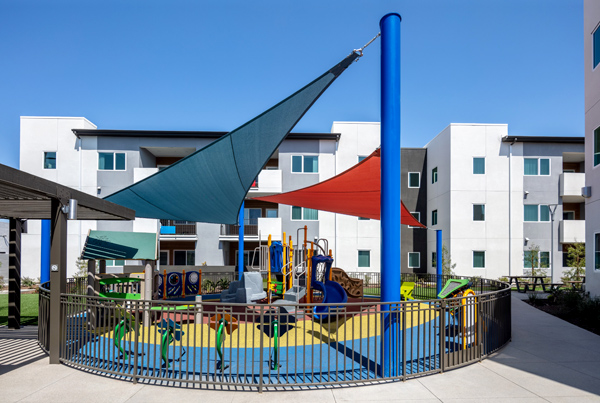 A fenced playground, shaded by colorful canopies mounted on poles.