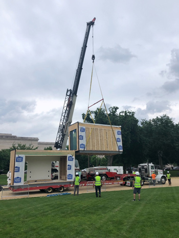 Photo of TOMU's Modular-volumetric housing components being delivered and lifted by crane off a semi-truck on the National Mall. Photo of TOMU's Modular-volumetric housing components being delivered and lifted by crane off a semi-truck on the National Mall.